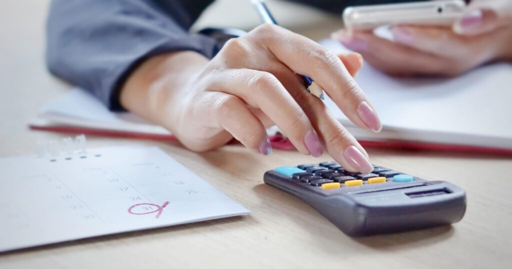 A person using a calculator while reviewing financial documents, with a calendar showing a circled due date. This image is representative of the financial planning and debt collection processes.